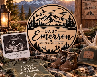 May include: A round wooden sign featuring a mountain, forest, and duck silhouette with the text Baby Emerson Arriving April 2027, an ultrasound photo labeled Our Greatest Adventure Yet, an olive green onesie, camouflage boots, and a Tiny Hunter cap.
