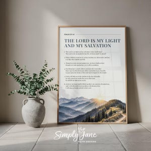 Può includere: Una stampa artistica verticale in una sottile cornice di legno con il testo Psalm 27:1-6, The Lord is my light and my salvation, e i versetti completi. La parte inferiore mostra un paesaggio di montagne blu e una foresta illuminata dal sole.
