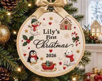 May include: A round embroidery hoop ornament featuring a beige fabric background with the text Lily's First Christmas 2026. Embroidered motifs include a snowman, gingerbread house, candy cane, penguin, polar bear, and red sleigh with a gold bow.