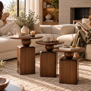 May include: A set of three dark brown wooden side tables, each featuring a circular tabletop supported by a central spherical element atop a rectangular pedestal base. The tables are arranged in a descending height order, showcasing a smooth, polished wood grain finish throughout their structural design.