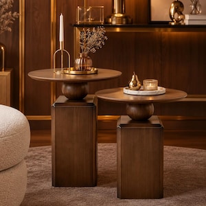 May include: Two dark brown wooden side tables, each featuring a circular tabletop supported by a central spherical element atop a rectangular pedestal base. The tables are arranged at different heights, displaying a smooth, polished wood finish.
