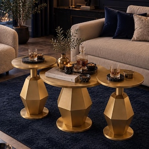 May include: A set of three round coffee tables with a metallic gold finish and geometric, faceted pedestal bases. The tables feature smooth, circular tabletops and are arranged in a cluster, providing a tiered surface for various decorative items.