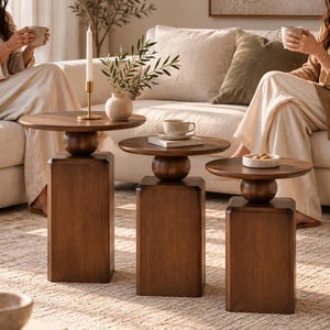 May include: A set of three nesting side tables made of dark brown wood, each featuring a circular tabletop supported by a spherical accent piece atop a rectangular base. The tables vary in height, arranged in a descending order from left to right.