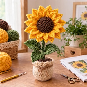 Könnte beinhalten: Eine gehäkelte Sonnenblume mit leuchtend gelben Blütenblättern und einer dunkelbraunen Mitte, befestigt an einem grünen Stiel mit zwei Blättern. Die Blume steht in einem beigen Häkeltopf, der mit einer kleinen Bindfaden-Schleife verziert ist.
