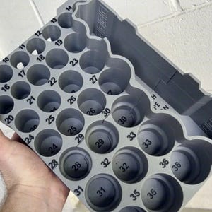 May include: A grey 3D-printed storage organiser featuring a grid of circular slots, each labelled with black numbers ranging from 8 to 36. The tray includes a rectangular compartment on the side with the text PEN embossed on the interior surface.