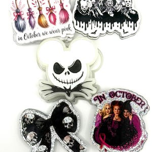 Könnte beinhalten: Eine Sammlung von fünf gestanzten Aufklebern mit verschiedenen Motiven: eine Reihe bunter Besen mit dem Text 'in October we wear pink', eine Gruppe von Horrorfilm-Bösewichten, ein weißer Jack Skellington-Kopf, eine schwarze Schleife mit Totenköpfen.