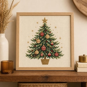 May include: A square framed cross-stitch embroidery featuring a green Christmas tree decorated with red and gold ornaments, a gold star topper, and small gold star accents, all set against a light beige fabric background in a light wood frame.
