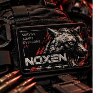 May include: A rectangular black patch featuring a graphic of a wolf head with bared teeth, red accents, and the text "SURVIVE ADAPT OVERCOME" and "NOXEN" in white lettering. The patch is attached to a black tactical vest with visible ammunition.