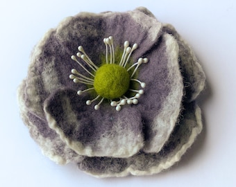 May include: A felted flower brooch in shades of grey and white with a green centre. The flower has a layered, ruffled appearance.