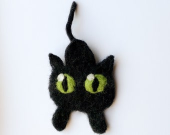 May include: A black felt cat with green eyes and a white nose. The cat is standing on its hind legs with its tail curled up.