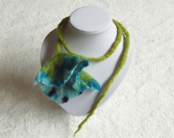 May include: A green and blue felted flower necklace on a white display stand. The necklace is made of wool and has a unique, organic shape.