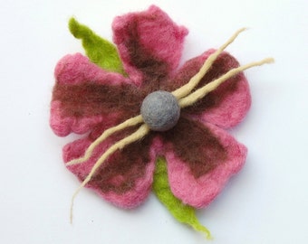 May include: A pink and brown felt flower with a grey felt centre and a beige felt stem. The flower is handmade and has a rustic, whimsical style.