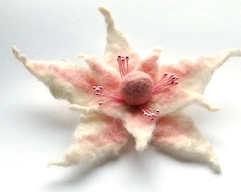 May include: A delicate, hand-felted flower brooch with a pink centre and white petals. The flower has a pink and white ombre effect and is accented with small pink beads.