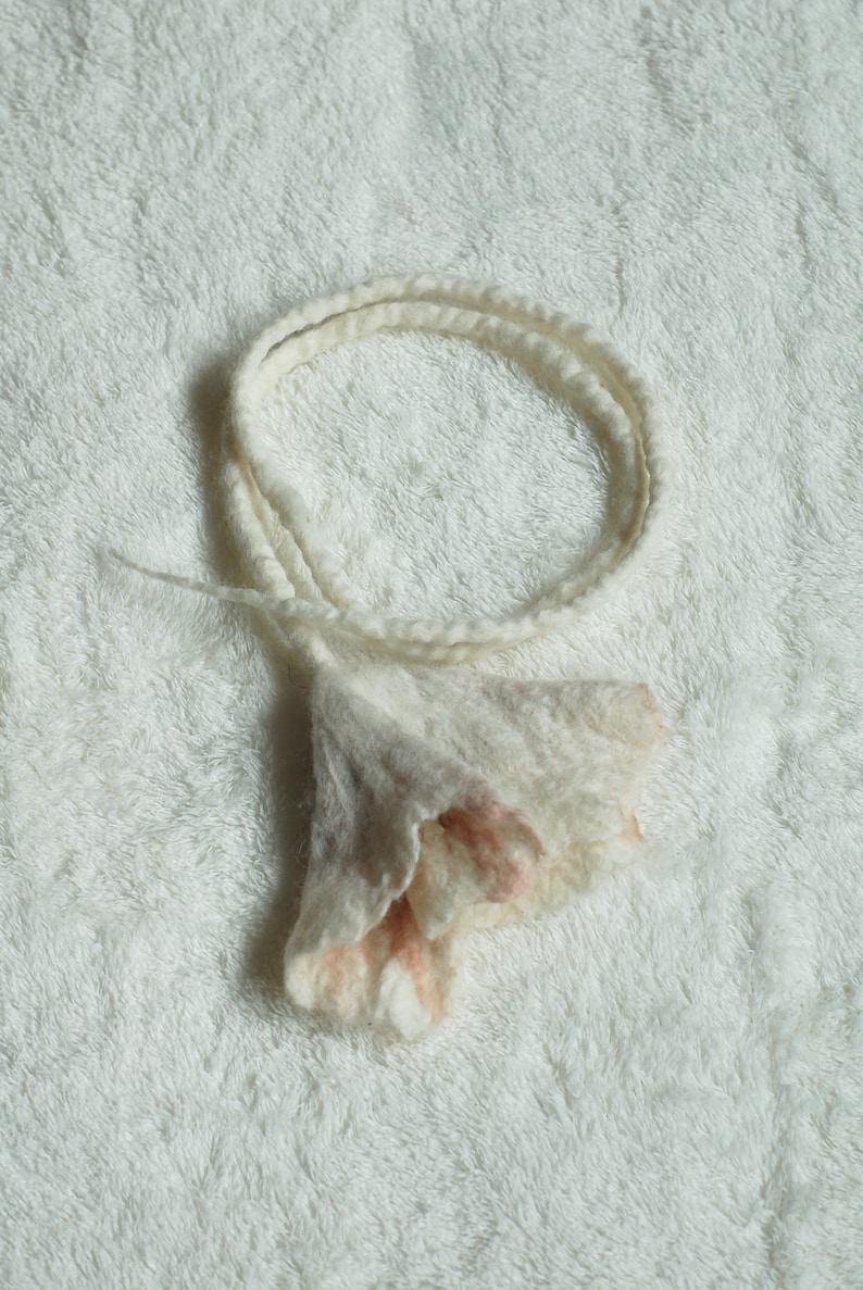 May include: A white and pink felted flower headband with a ruffled edge.
