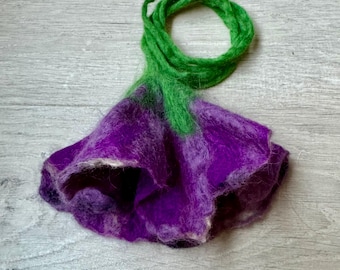 May include: A purple and green felted flower with a long green stem. The flower is made of wool and has a soft, fuzzy texture.
