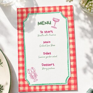 Op de afbeelding: Een rechthoekige menukaart met een rood en crème gingham rand en een groene geschulpte omlijsting. De tekst luidt: MENU, To start Buratta with Peaches, Main Grilled Sea Bass, Sides Summer garden salad, Dessert Berry pavlova, met roze illustraties.