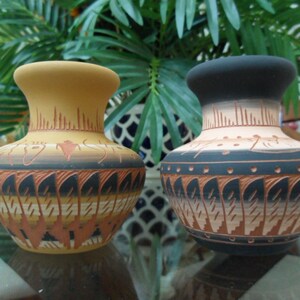 May include: Two decorative ceramic vases with a wide base and narrow neck. One vase is tan with black and orange patterns, the other is black and tan with orange patterns. Both vases have a similar shape and design, with intricate carved details.