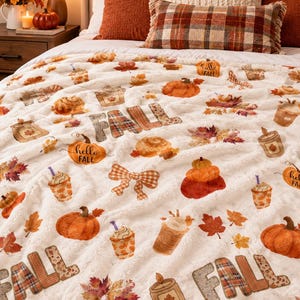 May include: A white plush throw blanket featuring a repeating pattern of orange pumpkins, autumn leaves, cinnamon rolls, candles, and plaid bows. The text "FALL" and "hello FALL" is printed in a brown and orange plaid pattern throughout.