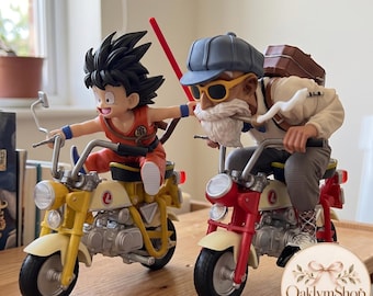 May include: Two anime character figurines riding small motorcycles. One figure has spiky black hair and an orange outfit on a yellow bike. The other figure has a white beard, blue cap, and sunglasses on a red bike. A red pole is held between them.