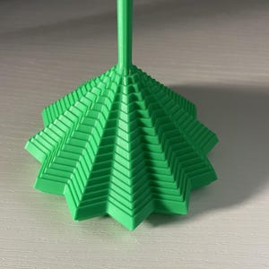 May include: A bright green, 3D-printed object featuring a wide, star-shaped base with tiered, geometric layers that taper upward into a thin, cylindrical stem. The structure displays a repeating, angular pattern across its surface.