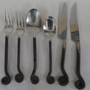 May include: Set of six handcrafted silverware pieces. The set includes two forks, two spoons, and two knives. The utensils have shiny silver heads and dark, wrought iron-style handles with a decorative swirl at the base.