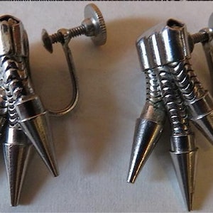 May include: A pair of silver tone clip-on earrings with a claw design. Each earring has three pointed claws.