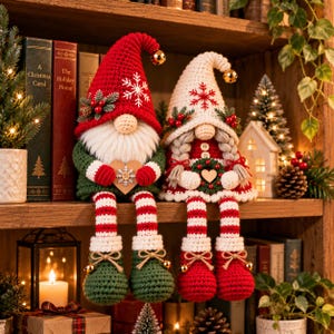 May include: Two crocheted gnome figurines sitting on a shelf. The left gnome wears a red hat with a white snowflake, green sweater, and striped legs. The right gnome has braided hair, a white hat with a red snowflake, and a red dress.