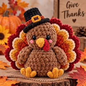 May include: A crocheted turkey plush toy featuring a brown body, a yellow beak, a red wattle, and black eyes with pink cheeks. The turkey wears a black top hat with an orange band and buckle, and has a fan-shaped tail with layers of red and yellow.
