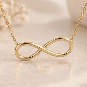 Puede incluir: Un collar de tono dorado con un colgante de símbolo de infinito pulido centrado en una delicada cadena de eslabones. El diseño de bucle suave y continuo del dije de infinito está elaborado con un acabado metálico reflectante y brillante.