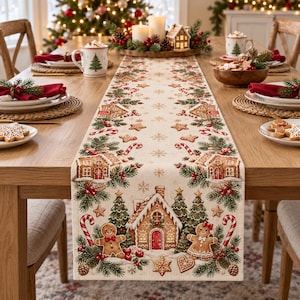 Op de afbeelding: Een crèmekleurige tafelloper met een herhalend kerstpatroon van peperkoekhuisjes, peperkoekmannetjes, zuurstokken, dennentakken, rode bessen en gouden sterren die over de lengte van de stof zijn gedrukt.