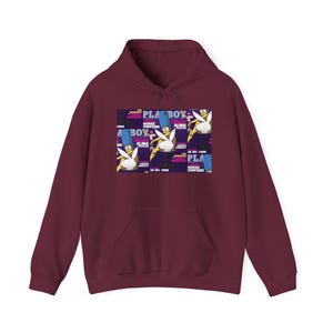 Puede incluir: Una sudadera con capucha de color granate y manga larga que presenta un estampado gráfico central. El diseño muestra varias imágenes repetidas de un personaje de dibujos animados con pelo azul alto y orejas de conejo blancas sobre un fondo morado.