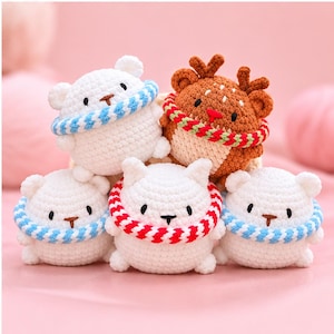 Può includere: Un gruppo di cinque piccoli animali di peluche all'uncinetto, di forma rotonda. Quattro sono bianchi con anelli al collo a righe blu e bianche, e uno è marrone con corna e un anello al collo a righe rosse e verdi. Occhi neri e naso ricamato.
