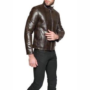 Puede incluir: Una chaqueta de color marrón oscuro con un patrón texturizado de piel de serpiente, que presenta un cuello alto, una cremallera frontal completa y mangas largas. La chaqueta se combina con pantalones negros lisos, creando un aspecto estructurado.