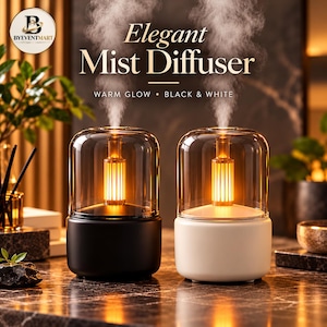 May include: Two cylindrical mist diffusers, one black and one white, each featuring a clear glass dome top and an internal glowing orange light element. Text above reads Elegant Mist Diffuser, WARM GLOW, BLACK & WHITE, and BYEVENTMART.