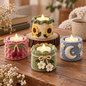 May include: Four cylindrical crochet candle holders with tea lights. One is pink with cherries, one is cream with sunflowers, one is sage green with white flowers, and one is blue with a crescent moon and stars. Each has a scalloped top edge.
