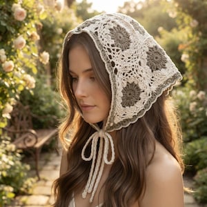 May include: A triangular crochet headscarf featuring a pattern of cream and sage green floral-inspired granny squares. The head covering is constructed with intricate openwork stitching and includes two long cream-coloured ties at the chin.