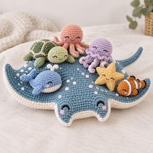 Op de afbeelding: Een grote gehaakte pijlstaartrog als basis voor verschillende kleine knuffels van zeedieren, waaronder een groene schildpad, een roze octopus, een paarse kwal, een blauwe walvis, een gele zeester en een oranje met witte clownvis.