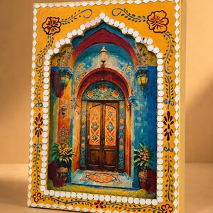 May include: A rectangular wall art piece featuring a painted scene of a wooden double door framed by an archway. The border is yellow with hand-painted floral motifs and small white mirror tiles. The scene includes blue walls, lanterns, and potted plants.