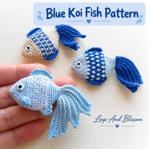 May include: Three crocheted koi fish appliques in shades of blue and cream. The text Blue Koi Fish Pattern and Loop And Blossom are visible. Each fish features a textured body, a prominent tail, and a small black and white eye detail.