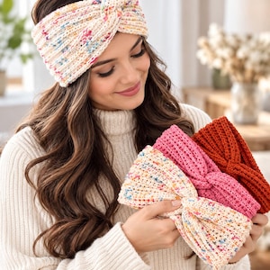 May include: A collection of three wide, ribbed knit headbands featuring a twisted front design. One headband is cream with multicolored speckles, one is solid bright pink, and one is a solid deep rust orange color, all made of soft yarn.
