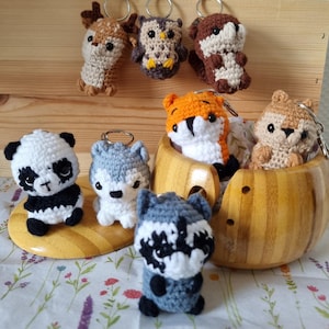 May include: A collection of small, handmade crochet animal keychains including a panda, wolf, raccoon, fox, deer, owl, otter, and squirrel. Each figure features detailed yarn stitching, black plastic eyes, and a metal keyring attached to the top.