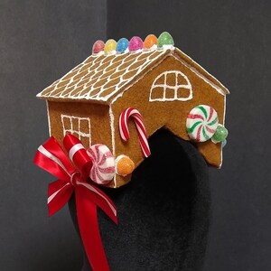 May include: A gingerbread house headband with red and white ribbon, candy canes, and colourful candies. The headband is on a black velvet mannequin head.