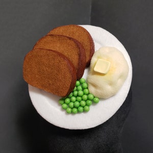 May include: A white plate with a brown bread, a white mashed potato with a yellow butter pat, and green peas.