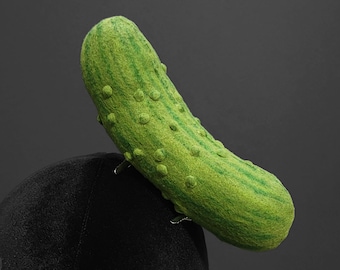 May include: A novelty hat featuring a large, green pickle design. The pickle has a textured surface with darker green stripes and small, round bumps. The hat is black and appears to be made of a soft material.