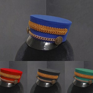 Op de afbeelding: Drie hoeden in verschillende kleuren, elk met gouden versieringen en een gouden ketting. De hoeden zijn blauw, rood en groen.