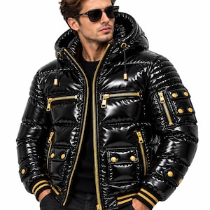 Op de afbeelding: Een glanzend zwart gewatteerd jack met een capuchon met trekkoorden, goudkleurige ritsen en gouden drukknopen op de zakken. Het jack is voorzien van geribbelde boorden met gouden strepen en een doorgestikt patroon over het geheel.