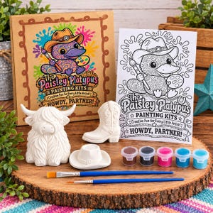 Pode incluir: Um kit de pintura com uma caixa de papelão e uma folha para colorir, ambos rotulados The Paisley Platypus Painting Kits Howdy, Partner!. Inclui uma vaca highland, uma bota, um chapéu de cerâmica branca, cinco potes de tinta e dois pincéis.