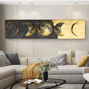 Peut inclure: Une œuvre d'art murale rectangulaire présentant une séquence horizontale de cinq phases lunaires. Le design passe d'un fond noir texturé avec des détails à la feuille d'or sur la gauche à une surface dorée unie sur le côté droit de la toile.