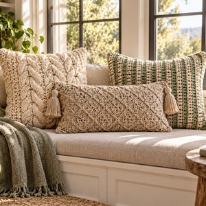 May include: A collection of three decorative throw cushions including one square cream cable-knit cushion, one rectangular beige cushion with a diamond pattern and side tassels, and one rectangular cushion featuring alternating green and cream stripes.