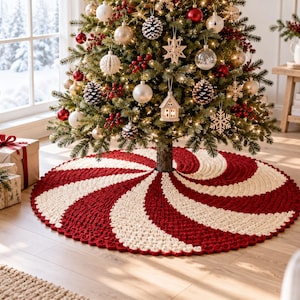 Puede incluir: Una falda circular de ganchillo para árbol de Navidad con un vibrante patrón de remolino de menta en hilo rojo oscuro y blanco crema. El tejido texturizado de puntadas gruesas irradia desde el centro creando un diseño en espiral.
